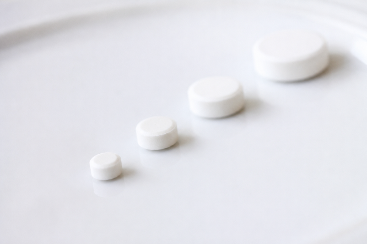 Graduated row of spironolactone tablets illustrating increasing dosage steps from 25mg to 200mg for acne treatment