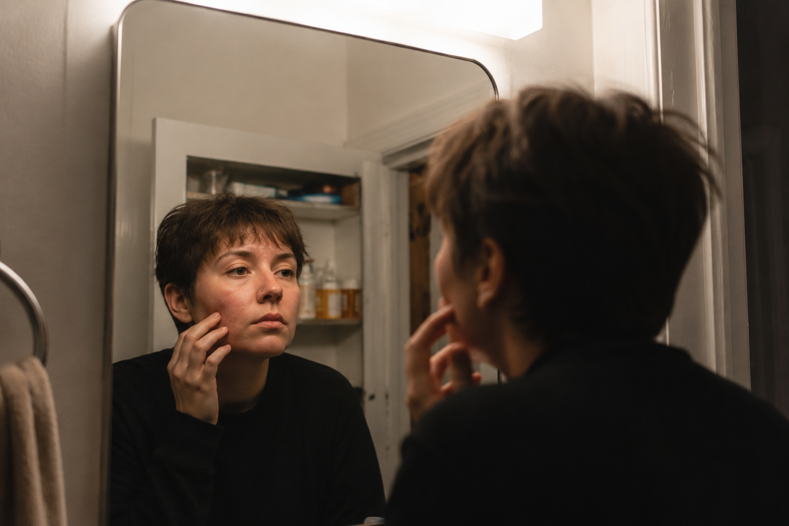 Person checking skin in bathroom mirror after stopping doxycycline acne treatment